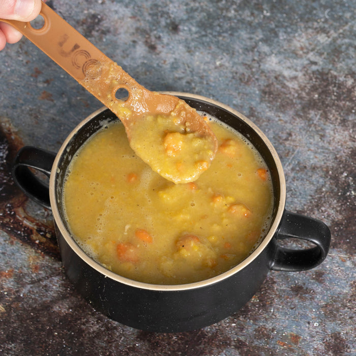 Hiker preparing Treko meal in the mountains - wooden spoon holding a portion of freeze-dried Boreal Pea Soup in black metal cup on rock in wilderness